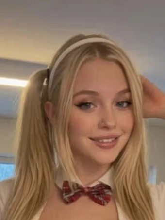 Porträt von Daisy, einer KI-Figur des Anbieters GoLove: blond, lächelnd, helles Zimmer.